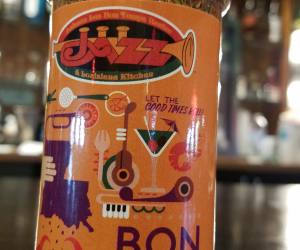 Jazz - A Louisiana Kitchen A bottle of BonTon Seasoning sits on a table, showcasing a vibrant label adorned with illustrations of a trumpet, crab, and drink against a softly blurred background. Kansas City, Columbia