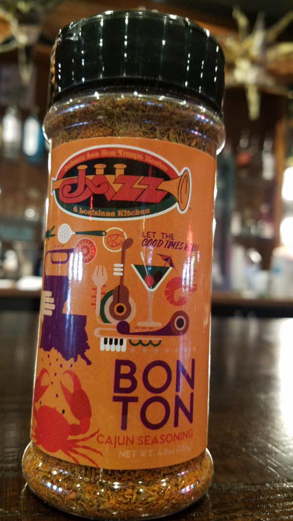Jazz - A Louisiana Kitchen A bottle of BonTon Seasoning sits on a table, showcasing a vibrant label adorned with illustrations of a trumpet, crab, and drink against a softly blurred background. Kansas City, Columbia