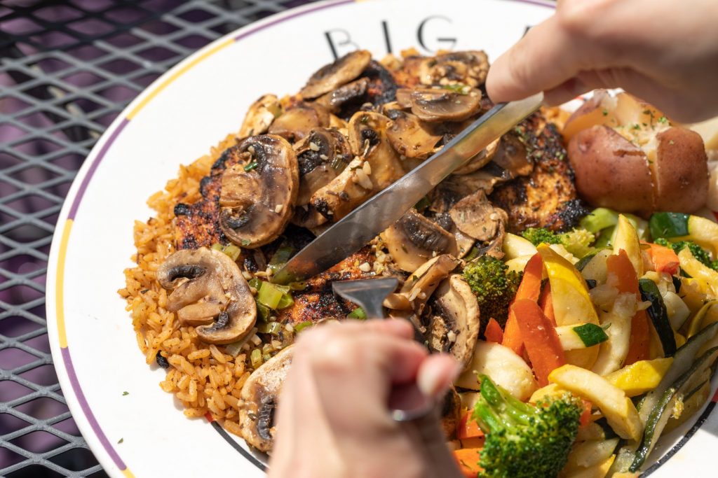 Jazz - A Louisiana Kitchen Person slicing mushroom-topped dish with rice, accompanied by mixed vegetables and potato on a plate. Kansas City, Columbia