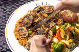 Jazz - A Louisiana Kitchen Person slicing mushroom-topped dish with rice, accompanied by mixed vegetables and potato on a plate. Kansas City, Columbia