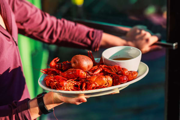 Jazz - A Louisiana Kitchen A person holding a plate of boiled crawfish, a potato, and a bowl of sauce. Kansas City, Columbia