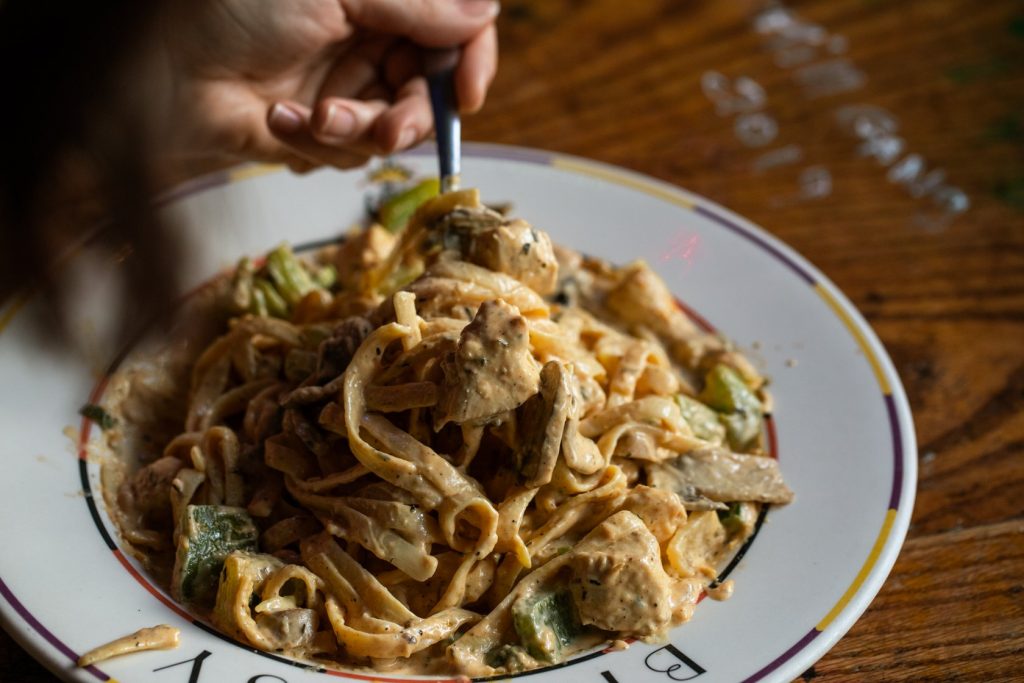 Jazz - A Louisiana Kitchen A hand twirls a forkful of creamy pasta containing chicken and vegetables on a decorative plate. Kansas City, Columbia