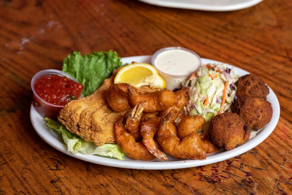 Jazz - A Louisiana Kitchen A plate with fried shrimp, fish, hush puppies, coleslaw, tartar sauce, and cocktail sauce on a wooden table. Kansas City, Columbia
