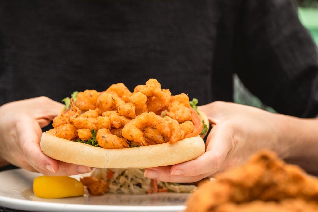Jazz - A Louisiana Kitchen Person holding a shrimp po' boy sandwich on a plate with a lemon wedge and side salad. Kansas City, Columbia