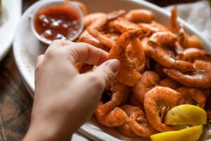Jazz - A Louisiana Kitchen A hand holding a seasoned shrimp over a plate of shrimp with lemon wedges, next to a small container of sauce. Kansas City, Columbia