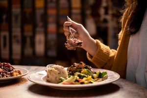 Jazz - A Louisiana Kitchen A person holds a forkful of meat over a plate with mashed potatoes, vegetables, and salad on a wooden table. Kansas City, Columbia