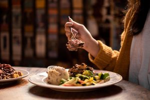 Jazz - A Louisiana Kitchen A person holding a forkful of food above a plate with mashed potatoes, vegetables, and meat in a cozy dining setting. Kansas City, Columbia