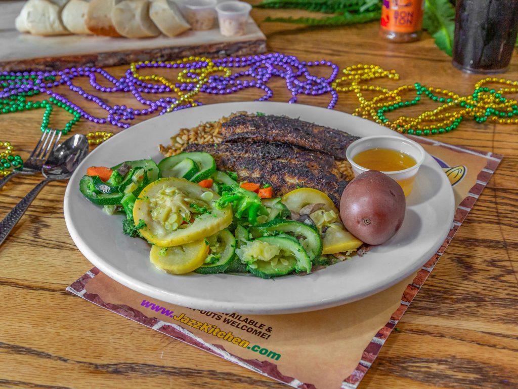 Jazz - A Louisiana Kitchen A plate of blackened fish with rice, steamed zucchini and squash, a boiled red potato, and a side of sauce. Mardi Gras beads are scattered on the table. Kansas City, Columbia