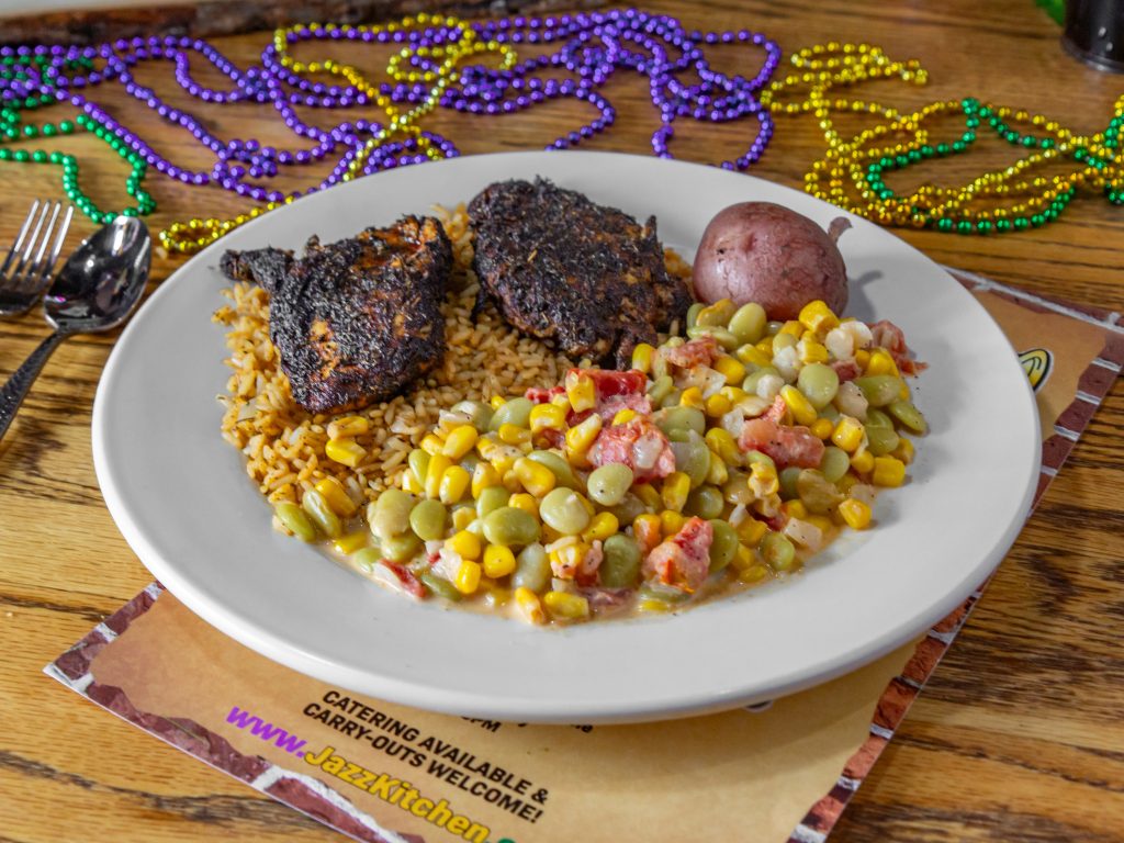 Jazz - A Louisiana Kitchen A plate of blackened chicken, rice, corn, lima beans, a red potato, and festive bead necklaces on a wooden table. Kansas City, Columbia