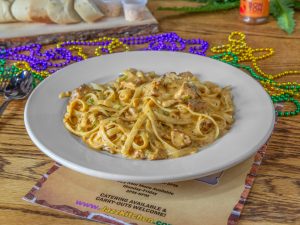 Jazz - A Louisiana Kitchen A plate of creamy pasta with herbs and meat on a wooden table, surrounded by colorful mardi gras beads, bread on a cutting board, and a silver spoon. Kansas City, Columbia