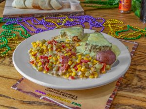 Jazz - A Louisiana Kitchen A plate of meatloaf with green sauce, corn and beans mix, and a small potato, surrounded by colorful Mardi Gras beads on a wooden table. Kansas City, Columbia