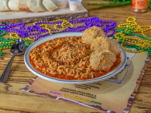 Jazz - A Louisiana Kitchen A plate of rice in tomato sauce with three breaded balls on the side, surrounded by colorful beaded necklaces on a wooden table. Kansas City, Columbia