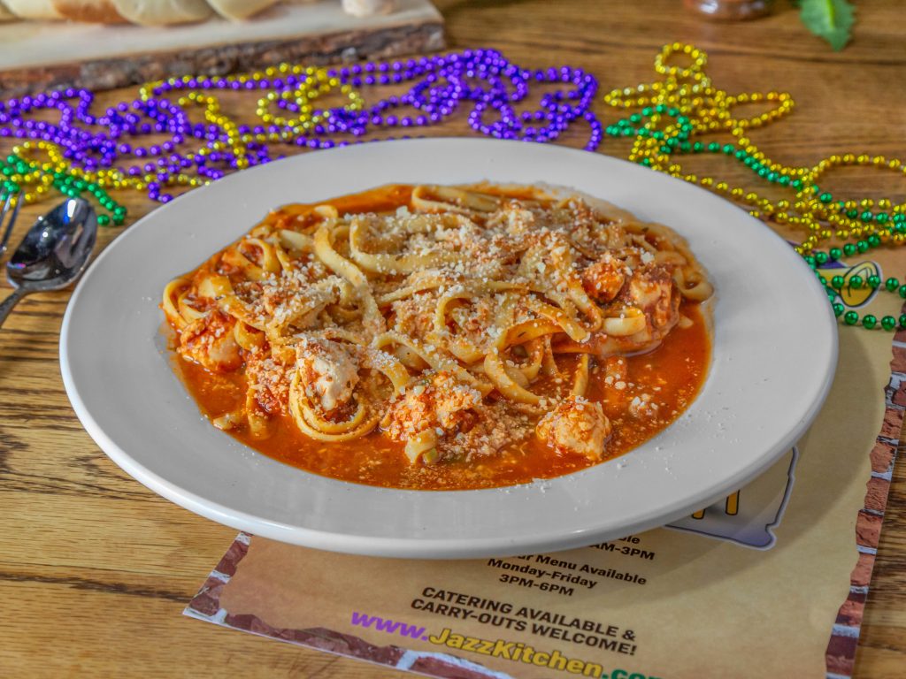 Jazz - A Louisiana Kitchen A plate of pasta with marinara sauce and grated cheese on a wooden table, surrounded by colorful beads. Kansas City, Columbia