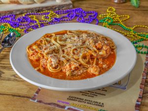 Jazz - A Louisiana Kitchen A plate of pasta with marinara sauce and grated cheese on a wooden table, surrounded by colorful beads. Kansas City, Columbia