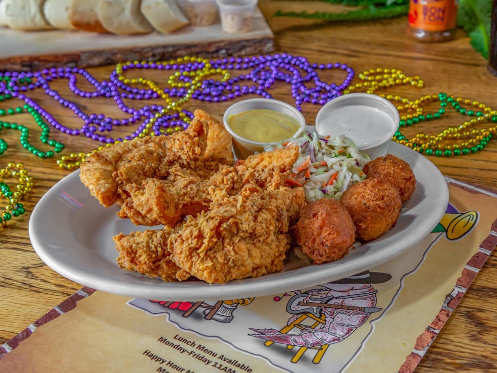 Jazz - A Louisiana Kitchen Plate of fried chicken, hush puppies, and coleslaw with two dipping sauces on a wooden table, surrounded by colorful Mardi Gras beads. Kansas City, Columbia, cajun food restaurant near me