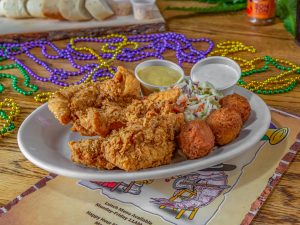Jazz - A Louisiana Kitchen Plate of fried chicken, hush puppies, and coleslaw with two dipping sauces on a wooden table, surrounded by colorful Mardi Gras beads. Kansas City, Columbia, cajun food restaurant near me