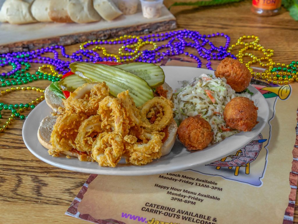 Jazz - A Louisiana Kitchen A plate of fried seafood with coleslaw, hush puppies, and pickles on a table decorated with colorful beads. Kansas City, Columbia