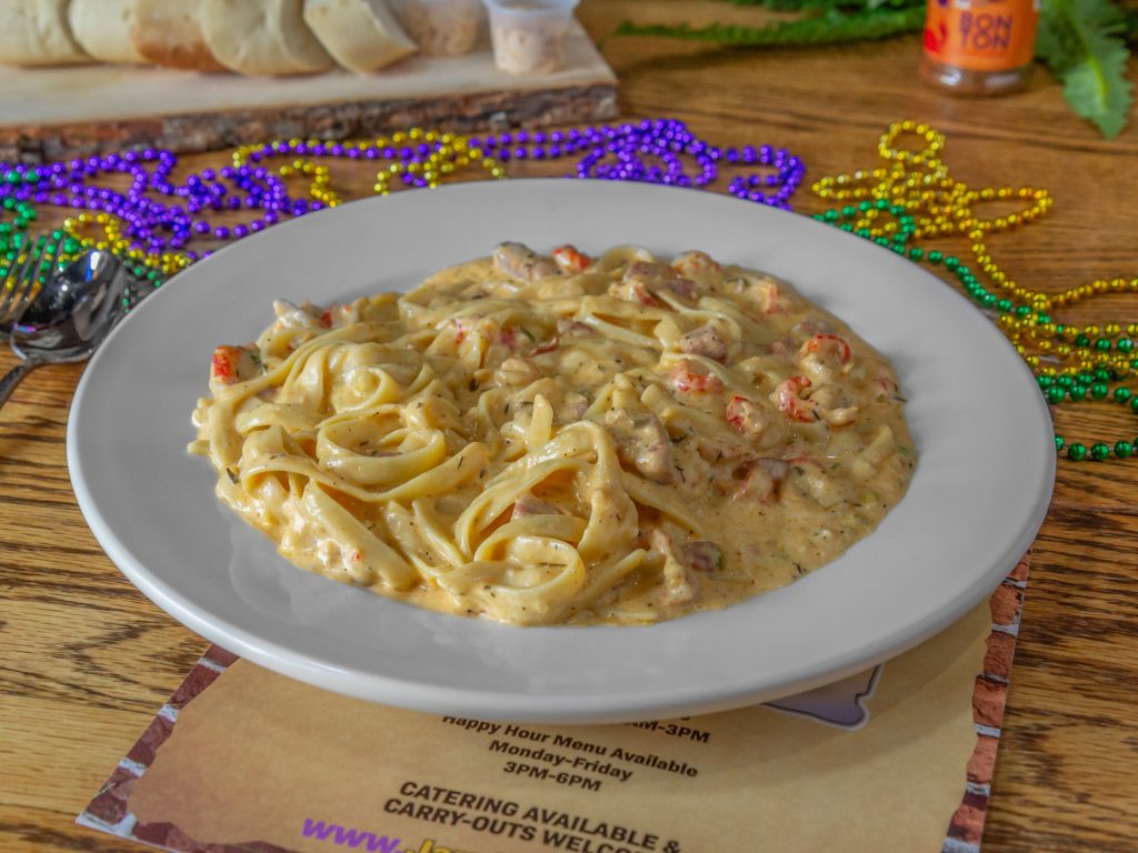 Jazz - A Louisiana Kitchen A plate of creamy pasta with seafood, garnished with sauce and served on a white dish. Mardi Gras beads and a menu are in the background. Kansas City, Columbia