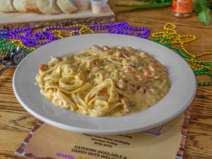 Jazz - A Louisiana Kitchen A plate of creamy pasta with seafood, garnished with sauce and served on a white dish. Mardi Gras beads and a menu are in the background. Kansas City, Columbia