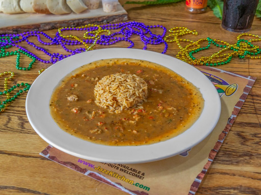 Jazz - A Louisiana Kitchen A plate of gumbo with a scoop of rice in the center, surrounded by colorful Mardi Gras beads on a wooden table. Kansas City, Columbia