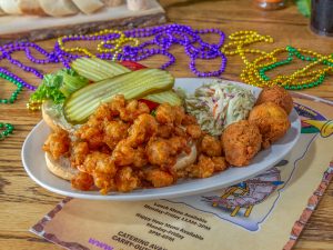 Jazz - A Louisiana Kitchen A plate with fried shrimp, coleslaw, pickle-topped sandwich bun, hush puppies, on a table decorated with Mardi Gras beads. Kansas City, Columbia
