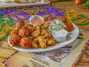 Jazz - A Louisiana Kitchen A plate of fried food with dipping sauces and coleslaw, surrounded by colorful Mardi Gras beads on a wooden table. Kansas City, Columbia