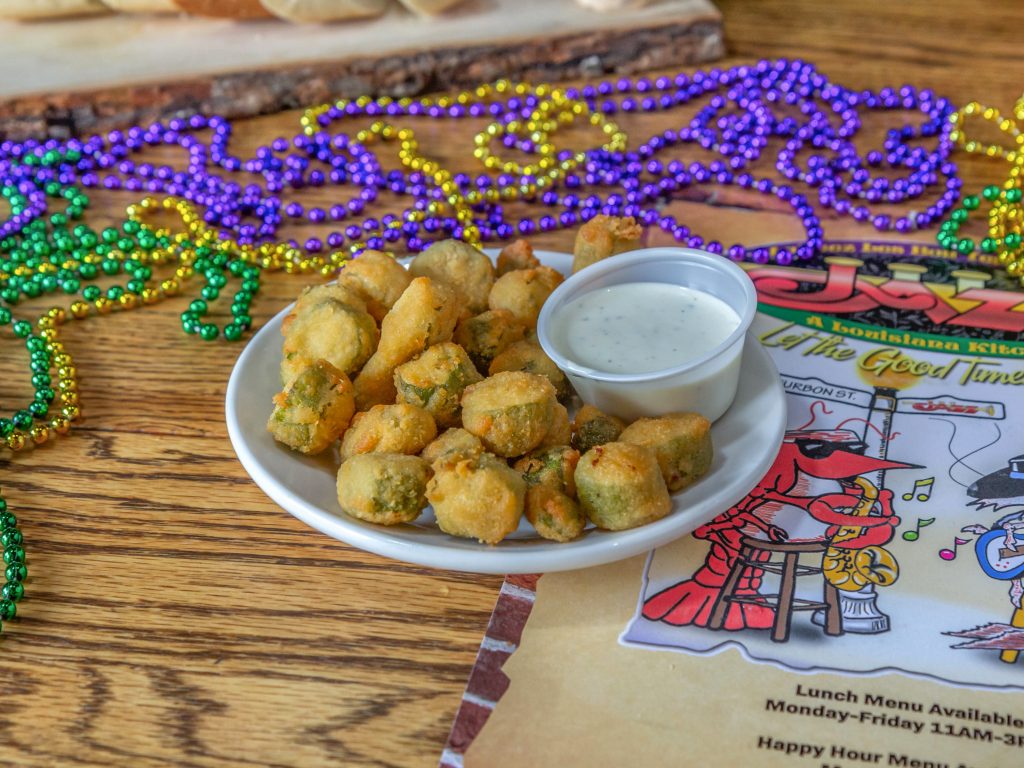 Jazz - A Louisiana Kitchen A plate of fried okra with dipping sauce on a wooden table, surrounded by colorful bead necklaces and a jazz-themed menu. Kansas City, Columbia