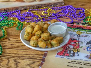 Jazz - A Louisiana Kitchen A plate of fried okra with dipping sauce on a wooden table, surrounded by colorful bead necklaces and a jazz-themed menu. Kansas City, Columbia