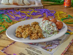 Jazz - A Louisiana Kitchen A plate with fried oysters, coleslaw, and hushpuppies on a table with Mardi Gras beads and a colorful menu underneath. Kansas City, Columbia