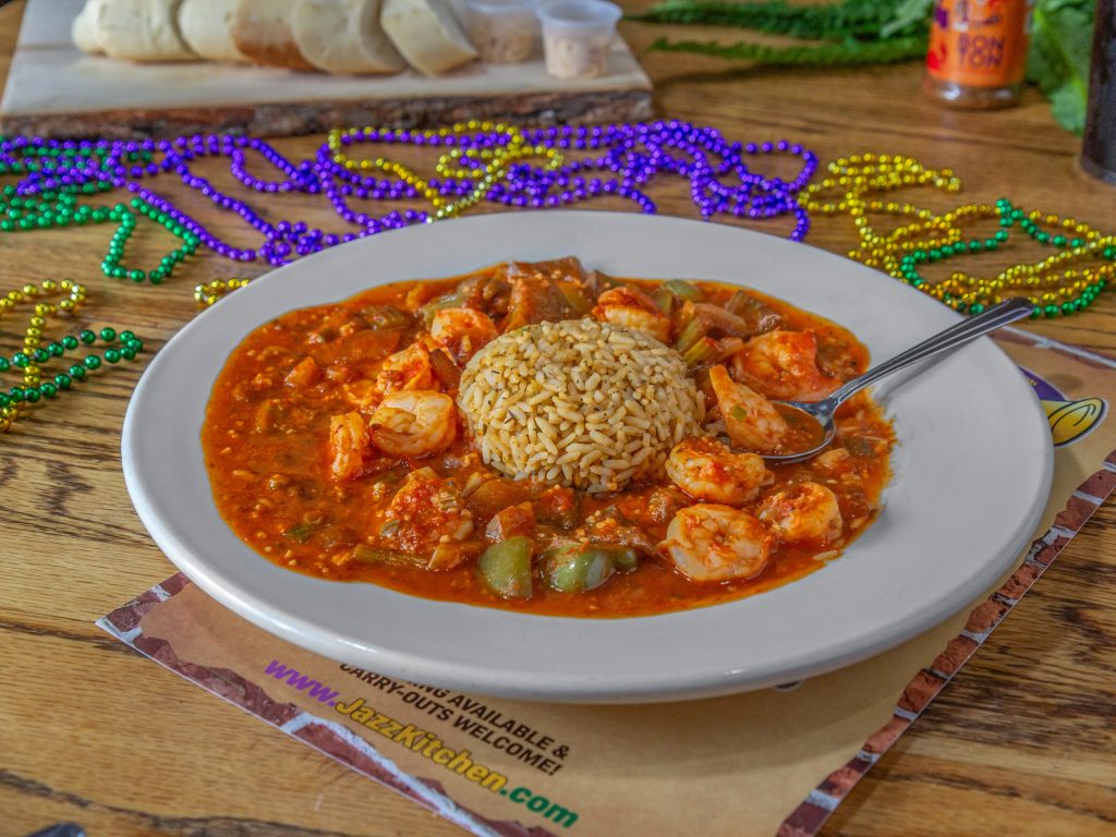 Jazz - A Louisiana Kitchen A plate of shrimp gumbo with rice in the center, surrounded by colorful Mardi Gras beads on a wooden table. Kansas City, Columbia