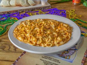Jazz - A Louisiana Kitchen A plate of creamy pasta with sauce on a wooden table, surrounded by colorful Mardi Gras beads and a menu underneath. Kansas City, Columbia