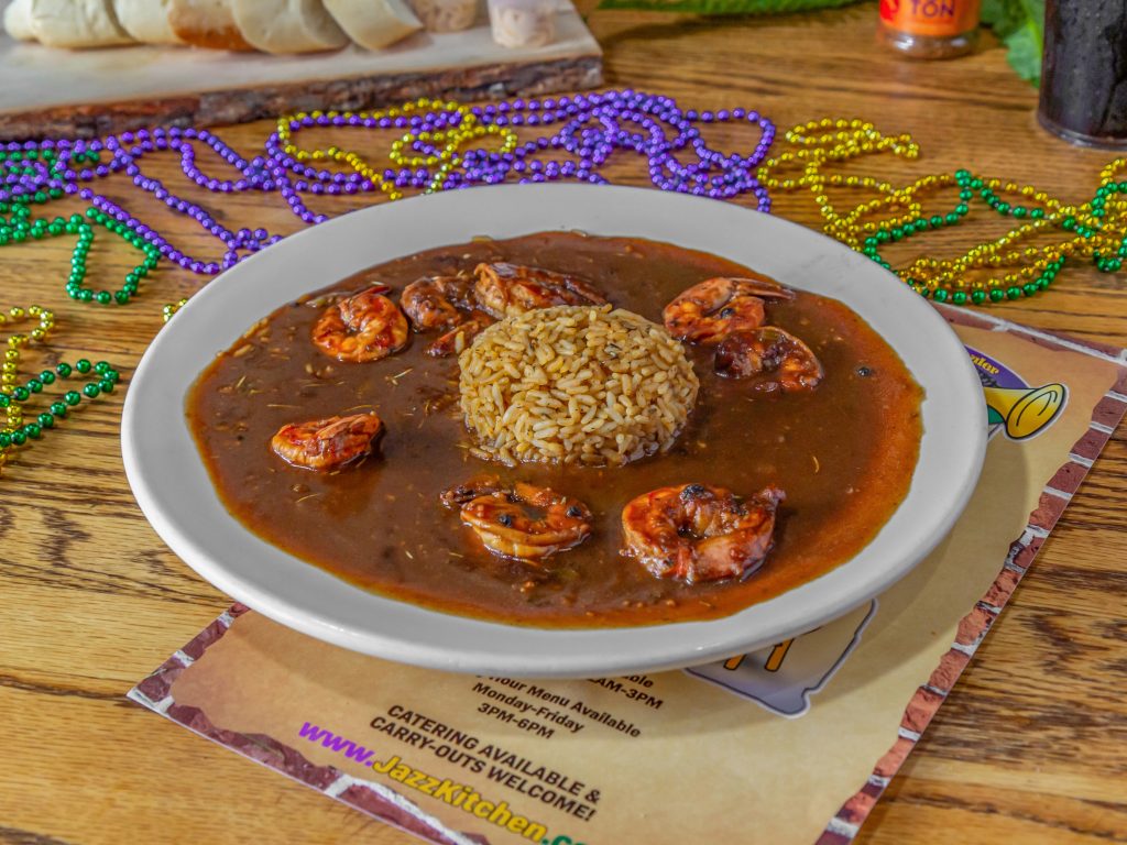 Jazz - A Louisiana Kitchen A plate of shrimp gumbo with rice in the center, surrounded by colorful Mardi Gras beads on a wooden table. Kansas City, Columbia