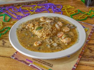 Jazz - A Louisiana Kitchen A plate of seafood gumbo with shrimp and rice, served on a table with colorful beaded necklaces around it. Kansas City, Columbia