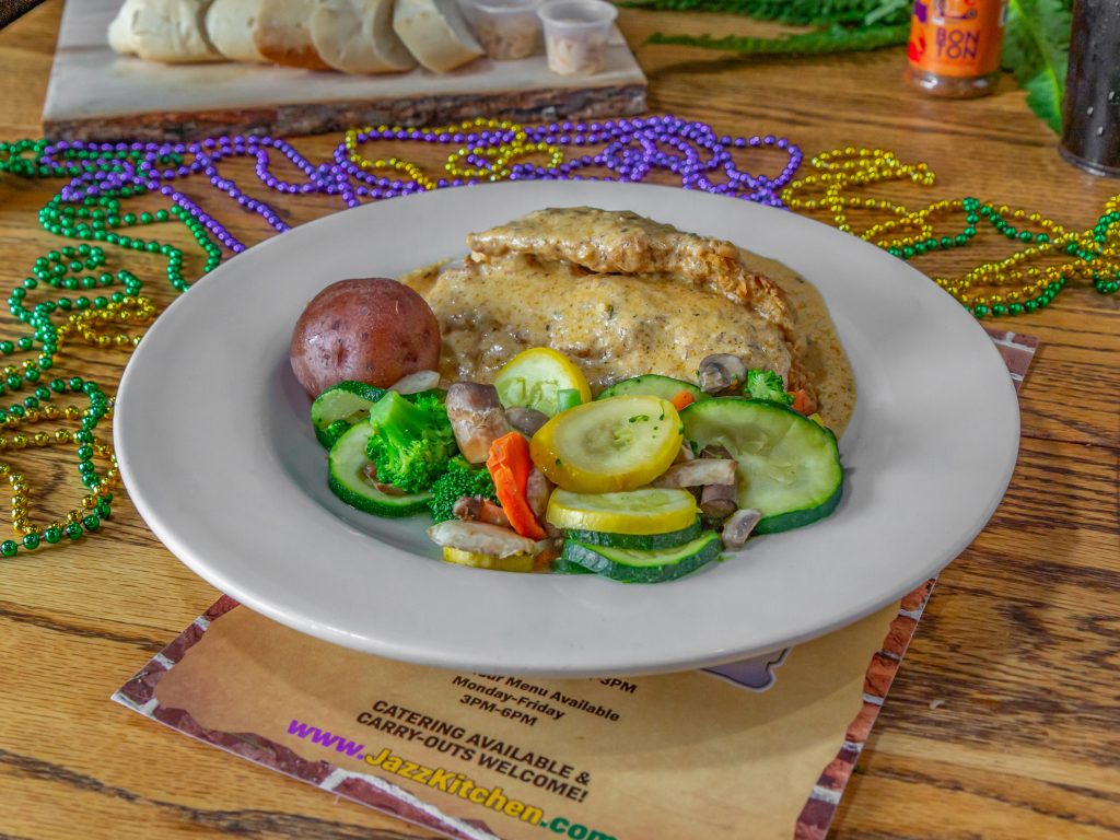 Jazz - A Louisiana Kitchen A plate of chicken with gravy, a red potato, and mixed vegetables. A colorful Mardi Gras bead necklace is on the wooden table. Kansas City, Columbia