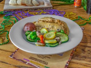 Jazz - A Louisiana Kitchen A plate of chicken with gravy, a red potato, and mixed vegetables. A colorful Mardi Gras bead necklace is on the wooden table. Kansas City, Columbia