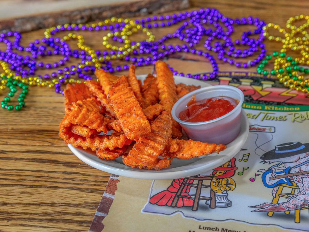 Jazz - A Louisiana Kitchen A plate of seasoned crinkle-cut fries with a side of ketchup is on a table, surrounded by colorful Mardi Gras beads and a restaurant menu. Kansas City, Columbia
