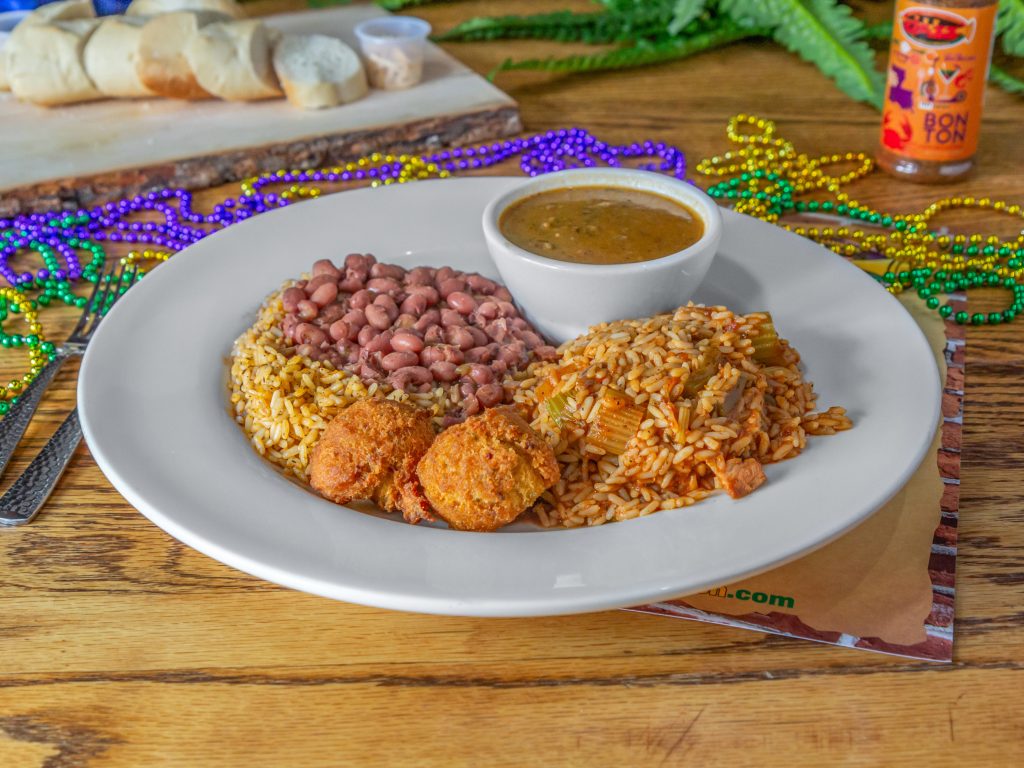 Jazz - A Louisiana Kitchen A plate with red beans, rice, hush puppies, and a bowl of sauce. Mardi Gras beads and sliced bread are in the background on a wooden table. Kansas City, Columbia