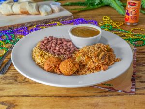 Jazz - A Louisiana Kitchen A plate with red beans, rice, hush puppies, and a bowl of sauce. Mardi Gras beads and sliced bread are in the background on a wooden table. Kansas City, Columbia