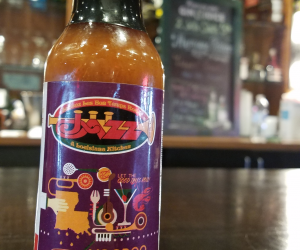 Jazz - A Louisiana Kitchen A bottle of Jazz Louisiana Kitchen Voodoo Juice hot sauce sits on a wooden table in a restaurant setting. Kansas City, Columbia, cajun food restaurant near me