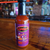 Jazz - A Louisiana Kitchen A bottle of hot sauce labeled "Voodoo Juice" on a wooden bar counter, with colorful lights in the blurred background. Kansas City, Columbia, cajun food restaurant near me