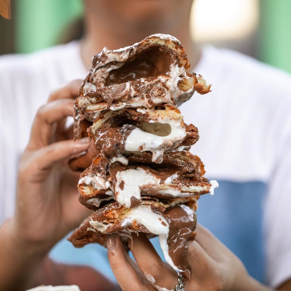 Jazz - A Louisiana Kitchen A person holds a large stack of pastries filled with melted chocolate and marshmallow, with gooey filling oozing out. Kansas City, Columbia, cajun food restaurant near me